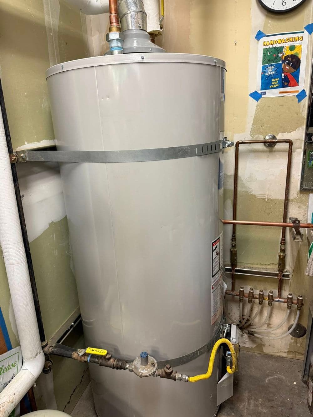 Residential hot water heater with plumbing connections in a utility room.